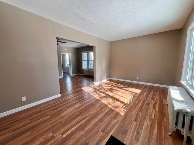 empty room with dark hardwood / wood-style flooring, a textured ceiling, and radiator heating unit