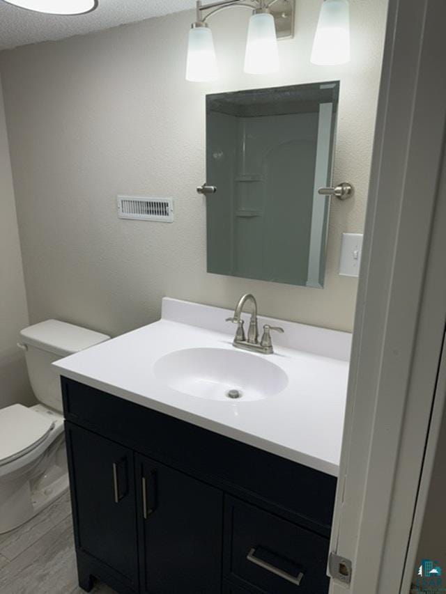 bathroom featuring wood-type flooring, vanity, walk in shower, a textured ceiling, and toilet