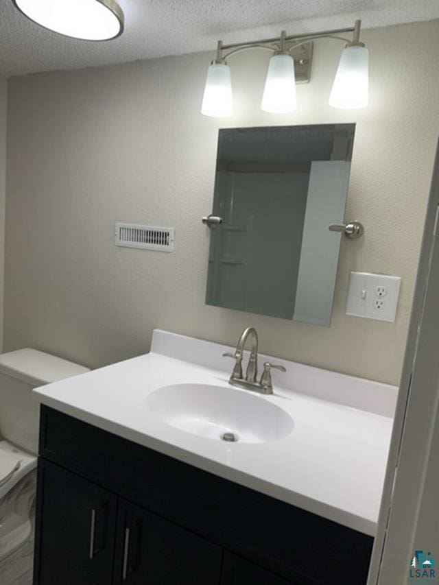 bathroom with a textured ceiling, toilet, and vanity