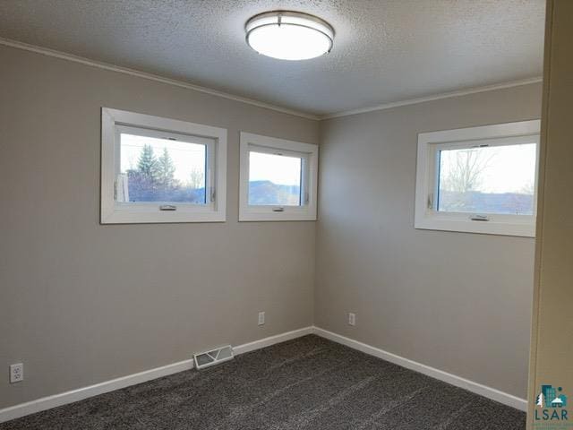 empty room with a wealth of natural light, crown molding, dark colored carpet, and a textured ceiling