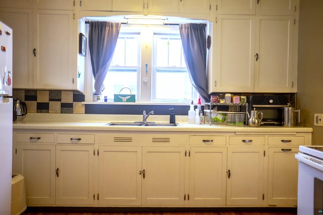 kitchen featuring sink, backsplash, white electric range oven, and white cabinetry