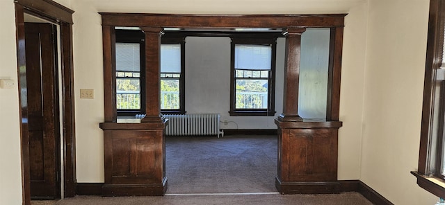 interior space featuring ornate columns, radiator heating unit, baseboards, and dark colored carpet