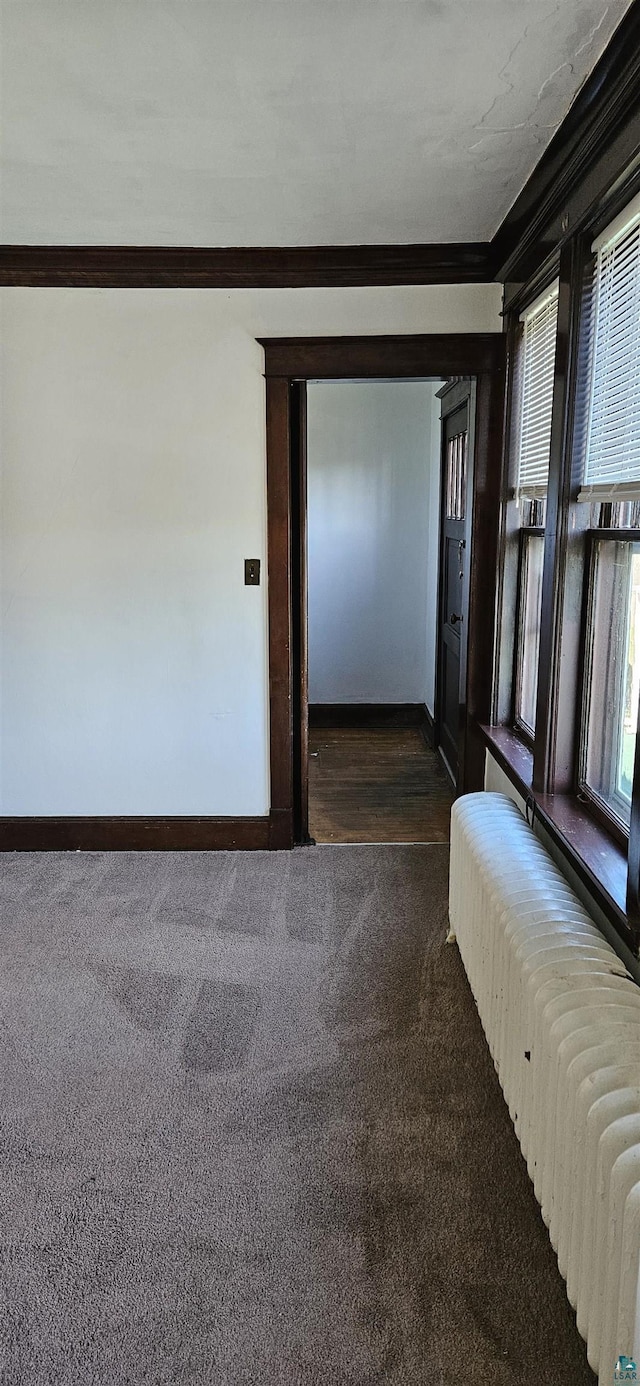 corridor featuring baseboards, dark colored carpet, radiator heating unit, and crown molding