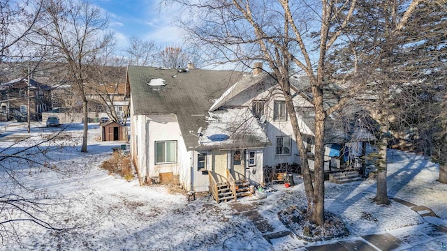 view of front of house featuring a shingled roof, an outbuilding, stucco siding, and a shed