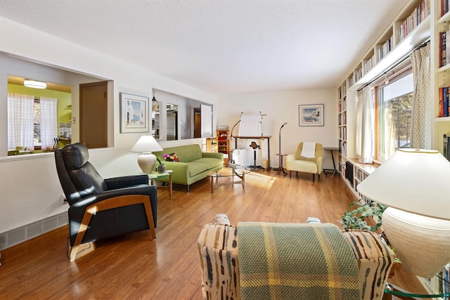 living room featuring baseboards, light wood-style flooring, visible vents, and a textured ceiling