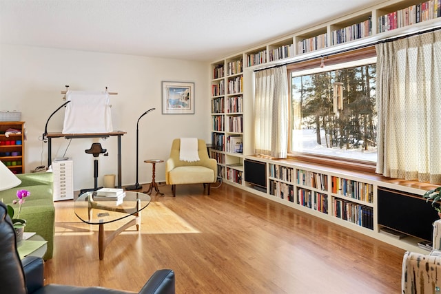 sitting room with wall of books, a textured ceiling, and wood finished floors