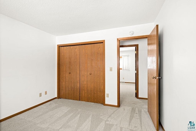 unfurnished bedroom featuring light carpet, a textured ceiling, baseboards, and a closet