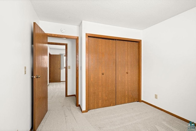 unfurnished bedroom featuring light carpet, a textured ceiling, baseboards, and a closet