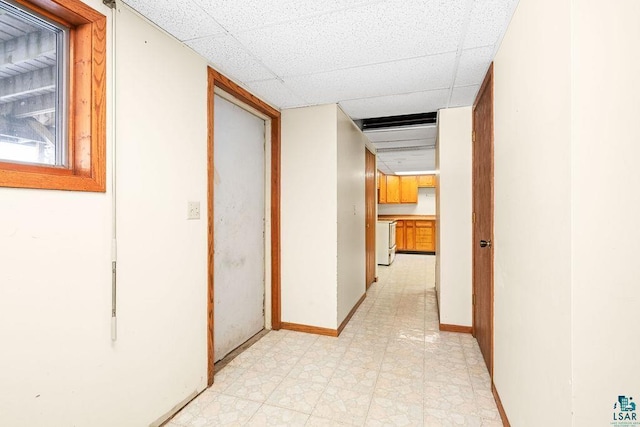 hallway with light floors, a drop ceiling, and baseboards