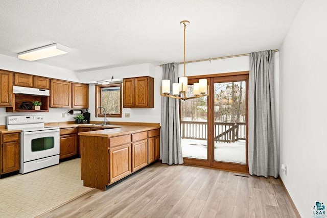 kitchen featuring electric range, hanging light fixtures, a peninsula, light countertops, and under cabinet range hood