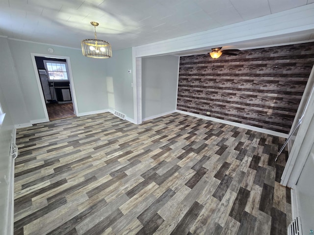 interior space with ceiling fan with notable chandelier, wood walls, visible vents, baseboards, and dark wood finished floors