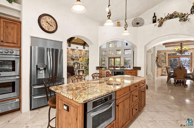 kitchen with a kitchen island with sink, appliances with stainless steel finishes, arched walkways, and a kitchen breakfast bar