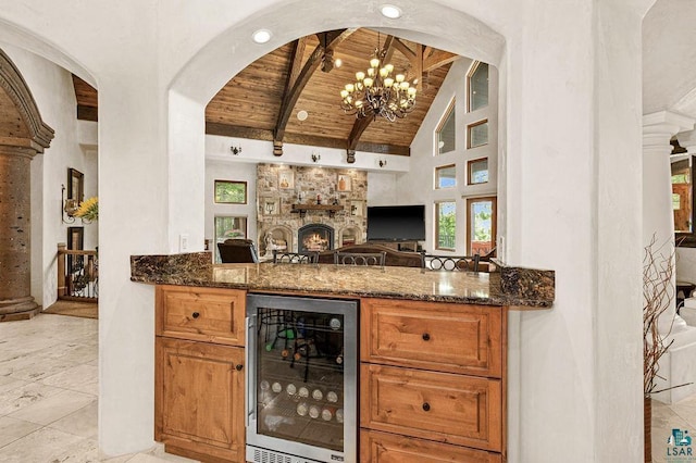 bar with high vaulted ceiling, wine cooler, a stone fireplace, wood ceiling, and beam ceiling