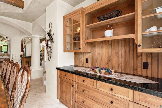 kitchen featuring arched walkways, dark countertops, glass insert cabinets, ornate columns, and open shelves