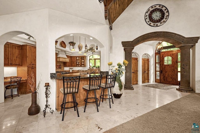 interior space with arched walkways, brown cabinetry, dark countertops, a towering ceiling, and a peninsula