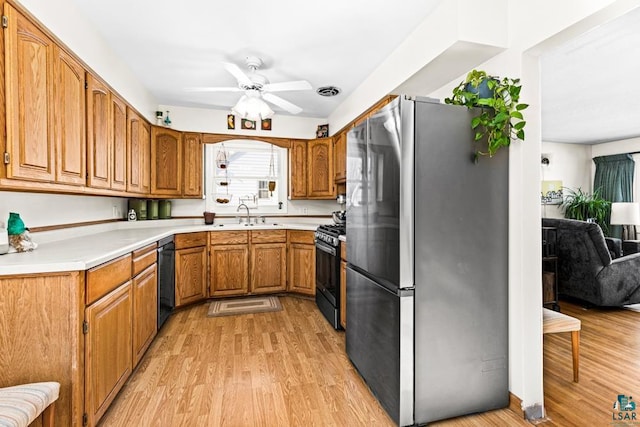 kitchen with light wood finished floors, light countertops, black gas range, freestanding refrigerator, and a sink