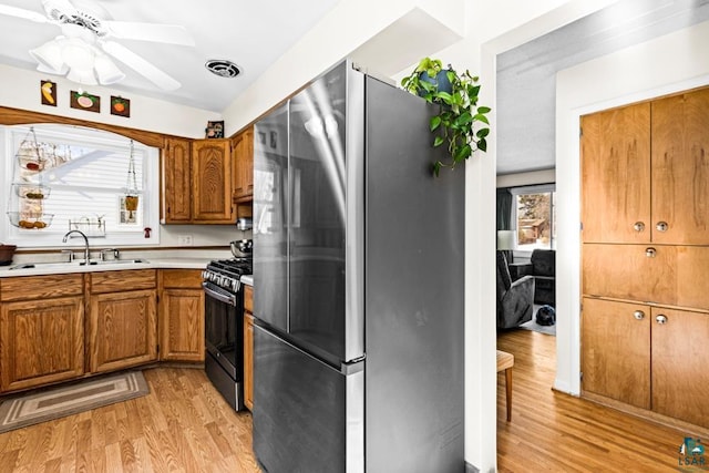 kitchen with a sink, light countertops, freestanding refrigerator, brown cabinetry, and gas range