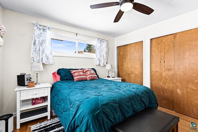 bedroom featuring multiple closets, a ceiling fan, dark wood-type flooring, and a textured ceiling