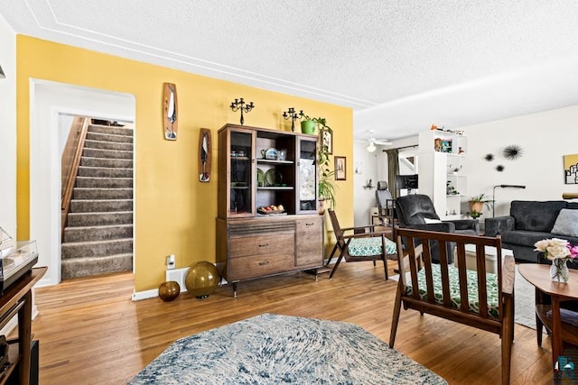 living area featuring stairway, a ceiling fan, a textured ceiling, wood finished floors, and baseboards