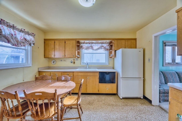 kitchen with a sink, black dishwasher, light countertops, freestanding refrigerator, and brown cabinetry