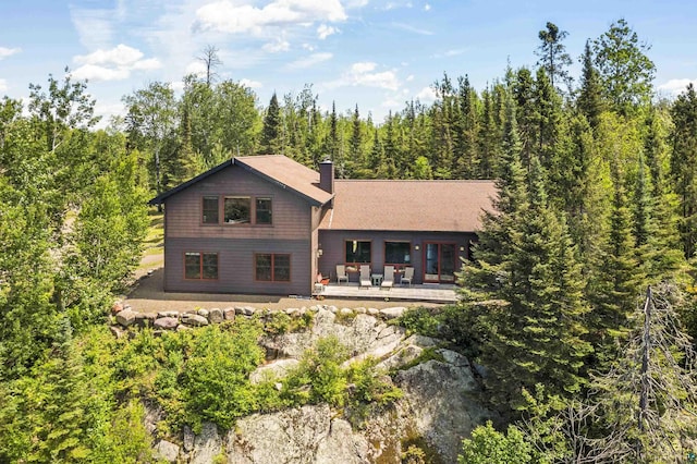 rear view of property featuring a forest view, a chimney, and a patio