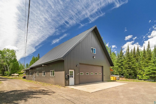 view of property exterior featuring driveway, a garage, metal roof, and an outdoor structure