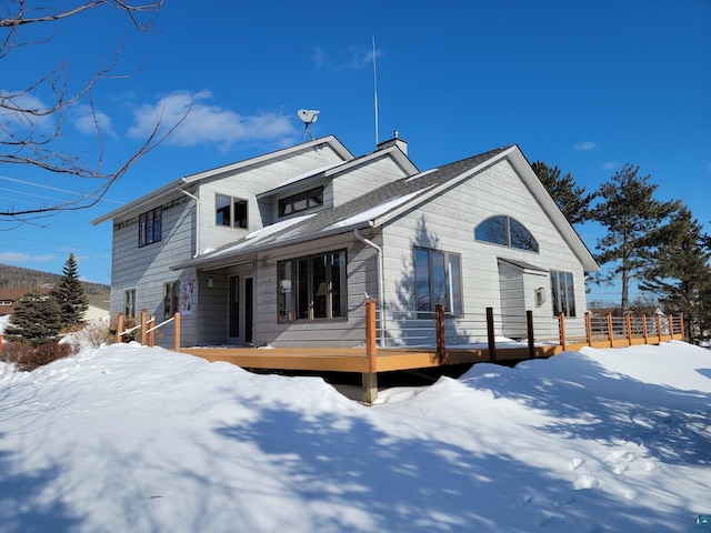 snow covered rear of property featuring a chimney and fence