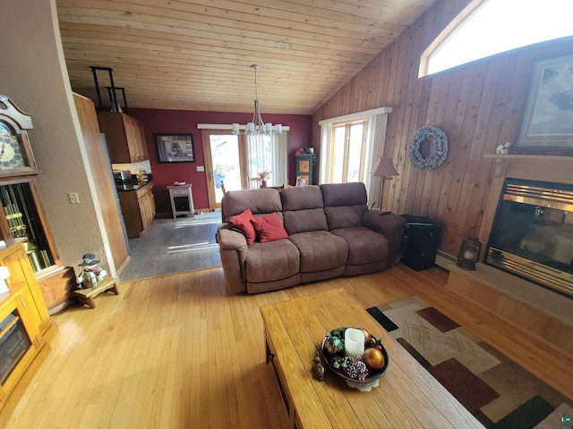 living area with lofted ceiling, a glass covered fireplace, light wood-style flooring, and an inviting chandelier