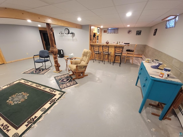 rec room with concrete block wall, a paneled ceiling, finished concrete flooring, and a dry bar