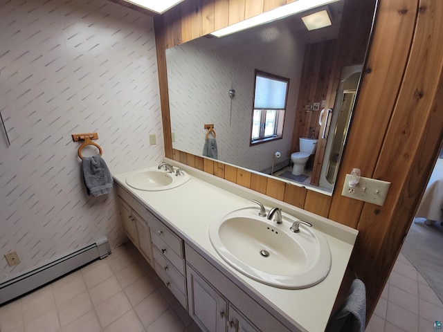 full bathroom featuring toilet, double vanity, a baseboard heating unit, and a sink