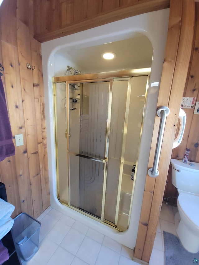 bathroom with a stall shower, wood walls, toilet, and tile patterned floors