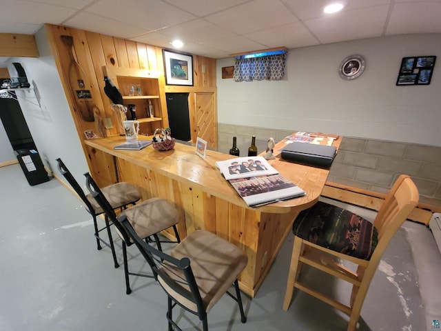 interior space with concrete block wall, finished concrete floors, a bar, and a paneled ceiling