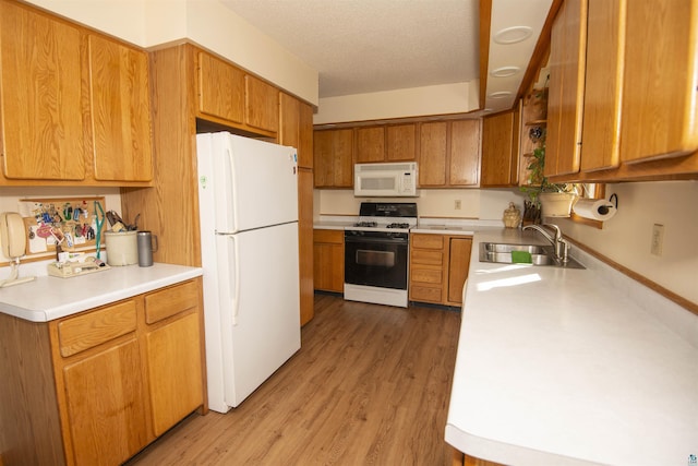 kitchen with brown cabinets, light countertops, light wood-style floors, a sink, and white appliances