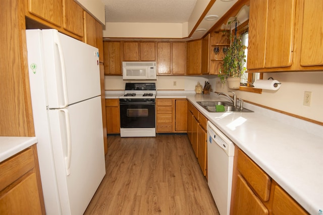 kitchen with white appliances, brown cabinetry, light countertops, light wood-style floors, and a sink