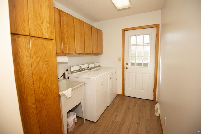 laundry room featuring a sink, baseboards, light wood-style floors, cabinet space, and washing machine and clothes dryer