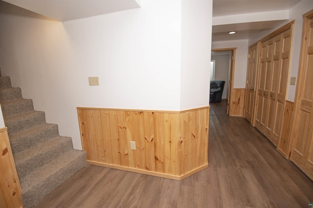 corridor featuring a wainscoted wall, dark wood-type flooring, stairs, and wooden walls