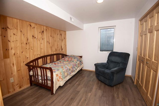 bedroom with wood walls, baseboards, visible vents, and dark wood-style flooring