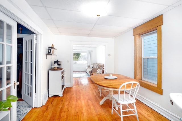 dining room with light wood-type flooring, a paneled ceiling, and baseboards