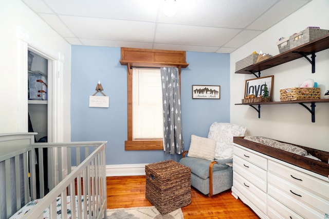 bedroom featuring a paneled ceiling, light wood-style flooring, baseboards, and a crib