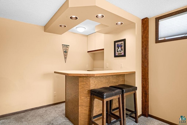 bar featuring a textured ceiling, recessed lighting, light carpet, bar, and baseboards