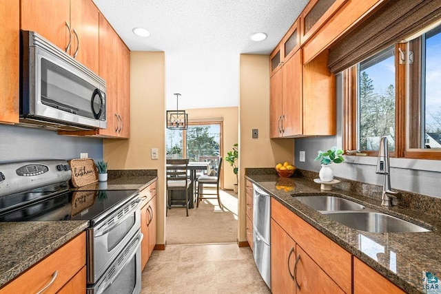 kitchen with pendant lighting, brown cabinets, stainless steel appliances, glass insert cabinets, and a sink