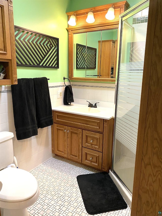 bathroom with toilet, vanity, a shower stall, and tile walls