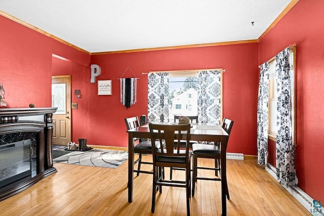 dining room featuring baseboard heating, ornamental molding, a glass covered fireplace, light wood-type flooring, and baseboards