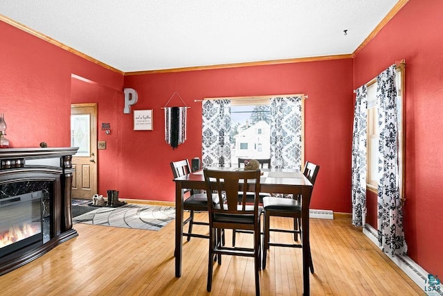 dining room featuring baseboards, baseboard heating, light wood-type flooring, a glass covered fireplace, and crown molding