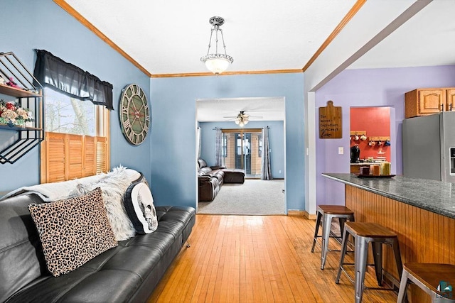 living room with light wood finished floors, ceiling fan, baseboards, and crown molding