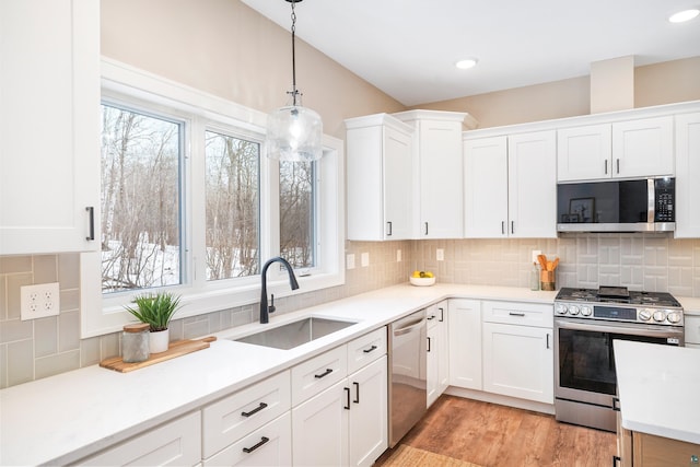 kitchen featuring pendant lighting, stainless steel appliances, light countertops, white cabinetry, and a sink