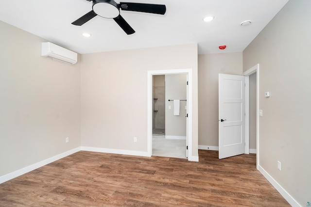 unfurnished bedroom with a wall unit AC, baseboards, and wood finished floors