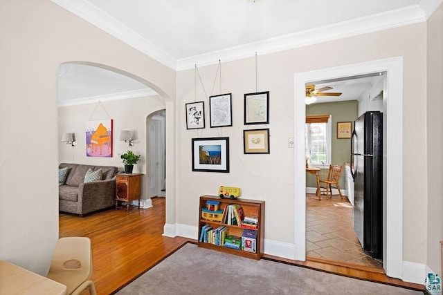 interior space with baseboards, arched walkways, crown molding, and wood finished floors