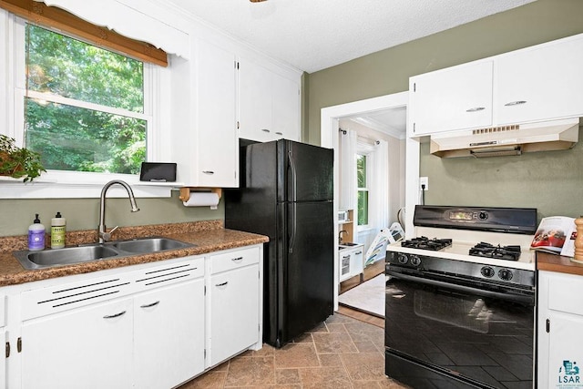 kitchen with gas range oven, freestanding refrigerator, stone finish floor, a sink, and under cabinet range hood