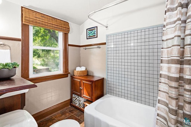 full bathroom with a wainscoted wall, tile walls, toilet, vaulted ceiling, and tile patterned flooring